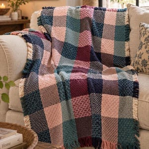 Peut inclure: Un jeté de canapé tissé présentant un grand motif à carreaux dans des tons de rose, bleu sarcelle, bleu marine et bordeaux. La couverture présente un motif en relief texturé dans chaque carré et est finie avec des franges couleur crème.