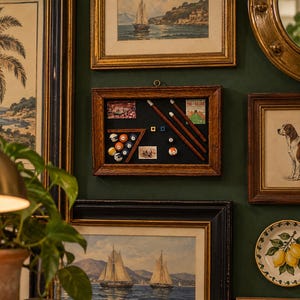 May include: A rectangular wooden shadow box frame containing a miniature billiards set. The display features a wooden triangle rack with coloured billiard balls, three miniature pool cues, two small square cubes, and two vintage-style rectangular cards.