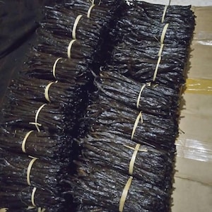 May include: Several bundles of dark brown vanilla pods, secured with natural twine. The vanilla pods are stacked, displaying their deep colour and texture. The image emphasizes the natural presentation of the vanilla.