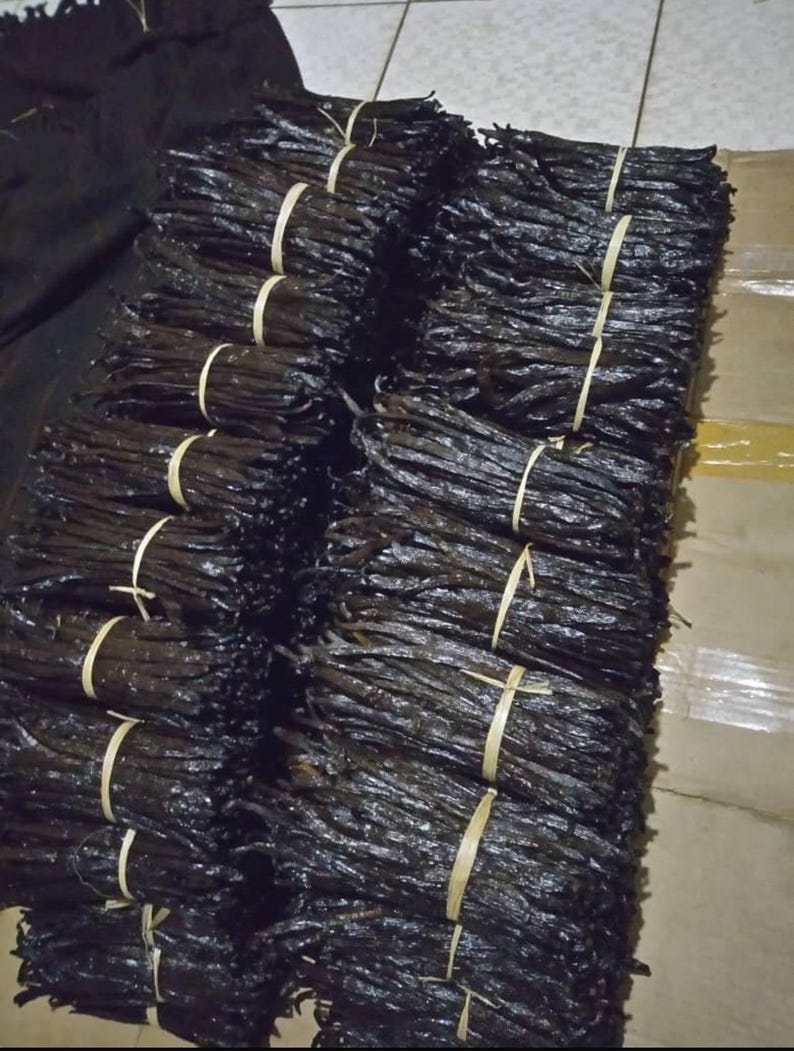 May include: Several bundles of dark brown vanilla pods, secured with natural twine. The vanilla pods are stacked, displaying their deep colour and texture. The image emphasizes the natural presentation of the vanilla.