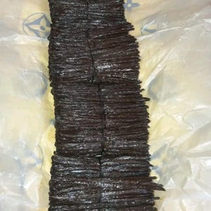 May include: Several bundles of dark brown vanilla pods tied with black twine. The pods are stacked on top of each other. The background is a white and yellow plastic sheet.
