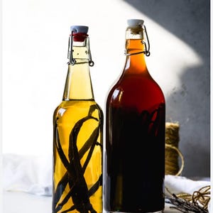 May include: Two glass bottles filled with liquid. One bottle contains a light yellow liquid with dark vanilla beans, and the other has a dark red liquid. Both bottles have swing-top closures.