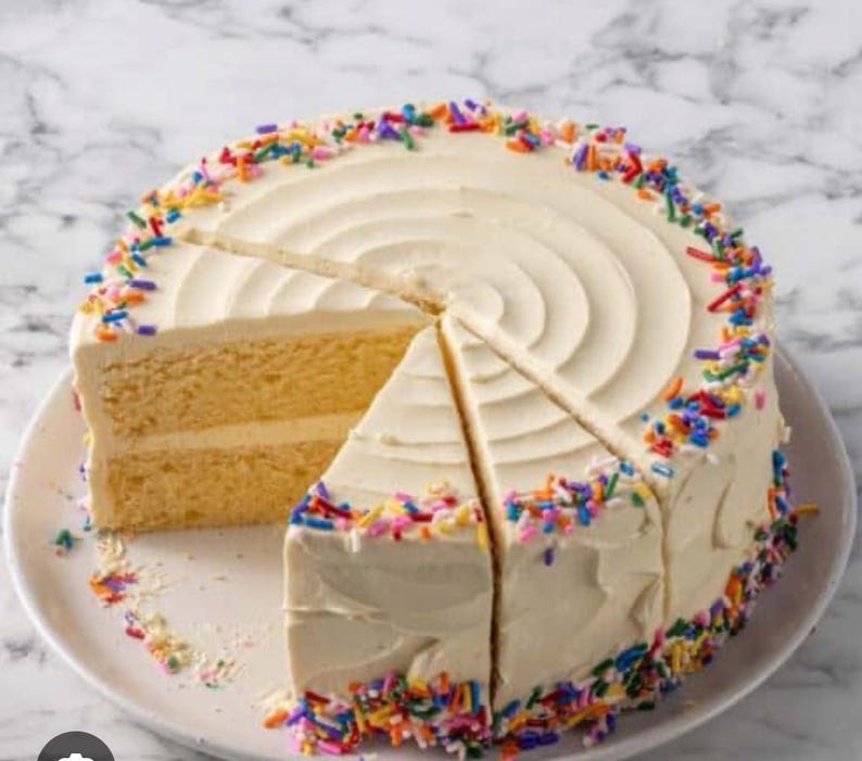 May include: A round cake with white icing and colourful sprinkles. A slice has been cut and removed, revealing the yellow cake layers. The cake sits on a white plate, ideal for a celebration.