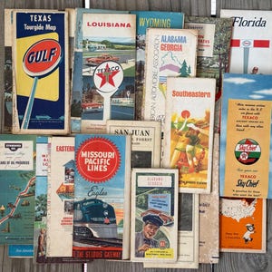 Può includere: Una collezione di mappe e brochure di viaggio vintage, con stati come Texas, Louisiana e Florida. Le mappe presentano design retrò con colori vivaci e loghi di marchi come Texaco e Gulf, che evocano viaggi su strada.