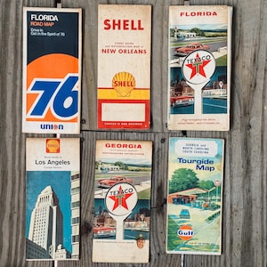 Può includere: Una collezione di mappe stradali e guide turistiche vintage, con marchi di stazioni di servizio come Shell, Texaco e Gulf. Le mappe presentano design retrò con colori vivaci e illustrazioni di auto classiche. Include una mappa stradale della Florida.