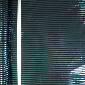 May include: A roll of fabric with horizontal stripes in teal and black. A white ruler is placed vertically on the fabric. The fabric has a shiny, textured appearance, with the stripes running across the width.