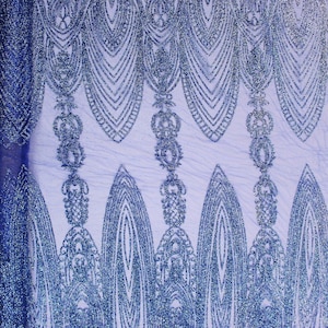 May include: Close-up of a blue fabric with a shimmering, glittery texture. The fabric features an intricate, symmetrical pattern of stylized teardrop shapes and ornate, vertical columns. The design is a deep blue color, creating a luxurious and elegant appearance.