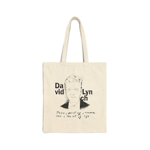 Può includere: Borsa tote color crema con uno schizzo in bianco e nero del volto di un uomo, con il nome "David Lynch" stampato sulla borsa. Sotto l'immagine, il testo recita "Musica, pittura, cinema, questa è l'arte della vita."