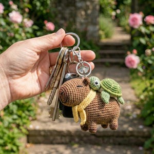 May include: A handmade brown crochet keychain featuring a capybara with a yellow scarf and a green turtle riding on its back. The keychain is attached to a silver keyring with several keys.
