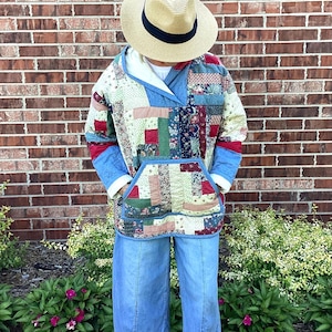 Puede incluir: Chaqueta con capucha de patchwork multicolor con un gran bolsillo delantero, combinada con pantalones vaqueros azul claro, un sombrero de paja y zapatillas blancas. La chaqueta presenta parches rojos, azules, verdes y crema. Fondo: pared de ladrillo.