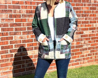 May include: A patchwork jacket in shades of green, black, cream, and blue. The jacket has a quilted design, long sleeves, and two front pockets. The model is wearing dark blue jeans and a white top.