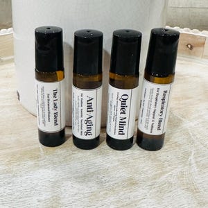 Könnte beinhalten: Vier ätherische Öl-Rollerflaschen mit schwarzen Kappen und Etiketten. Die Etiketten lauten: "The Lady Blend", "Anti-Aging", "Quiet Mind" und "Respiratory Blend". Die Flaschen sind braun und bernsteinfarben.