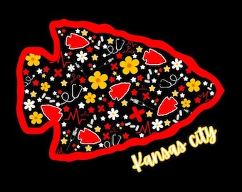 May include: A black graphic featuring a red arrowhead shape with a red outline. The arrowhead is filled with white stars, yellow and white flowers, red arrowheads, medical symbols, and the words "Kansas city" in yellow.
