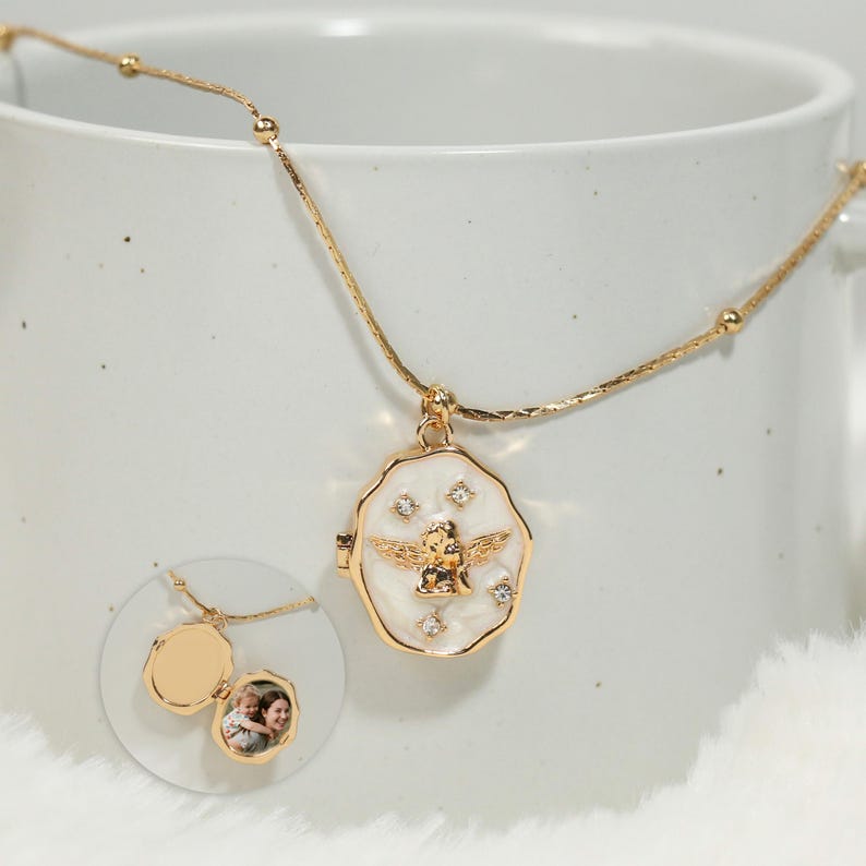 Pode incluir: Colar com pingente de medalh&atilde;o dourado com um design de anjo dourado e pequenos cristais. O medalh&atilde;o abre para revelar uma pequena foto. O colar &eacute; exibido em um fundo branco.