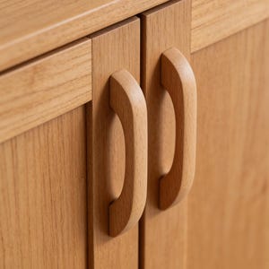 Puede incluir: Primer plano de un armario de madera clara con dos puertas. Cada puerta tiene un tirador curvo de madera. La veta de la madera es visible y el armario parece estar hecho de madera dura clara.
