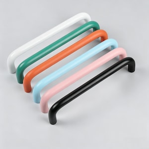 May include: Six cabinet handles in a row, each with a curved bar design. The handles are in a variety of colors: white, green, orange, light blue, pink, and black. The handles are made of a smooth, solid material.