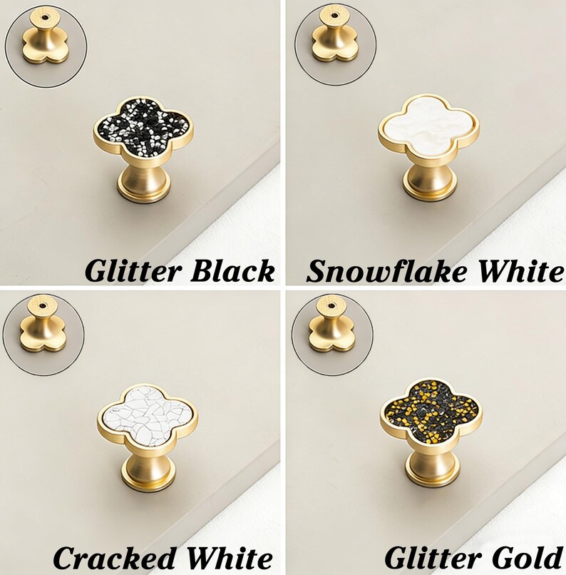 K&ouml;nnte beinhalten: Vier Schrankkn&ouml;pfe mit Kleeblatt-Design. Die Kn&ouml;pfe sind in vier verschiedenen Ausf&uuml;hrungen erh&auml;ltlich: Glitter Black, Snowflake White, Cracked White und Glitter Gold. Jeder Knopf hat einen goldfarbenen Sockel und eine dekorative Oberseite.