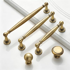 May include: A collection of antique brass cabinet hardware, including three different sizes of pull handles and two knob styles. The hardware has a warm, aged finish and a classic design, suitable for kitchen or bathroom cabinets.