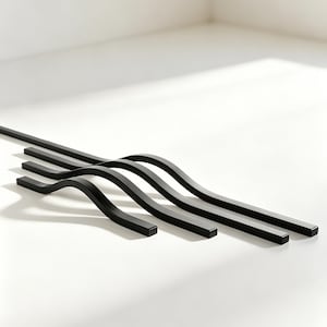 Puede incluir: Cuatro tiradores de armario de metal negro con un diseño curvo están dispuestos sobre una superficie blanca. Los tiradores tienen un acabado mate y proyectan sombras. El diseño es moderno y minimalista.