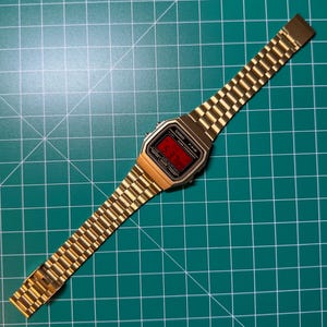 Peut inclure: Montre num&eacute;rique dor&eacute;e avec affichage rouge indiquant l'heure. Le bracelet est &eacute;galement dor&eacute;, avec un design &agrave; maillons classique. Le cadran affiche la marque "CASIO" et le mod&egrave;le "F-91W".