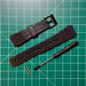 May include: Black watch band replacement kit. The kit includes a black watch band, a small screwdriver, and two gold-colored spring bars. The watch band is made of a flexible material and has multiple adjustment holes.