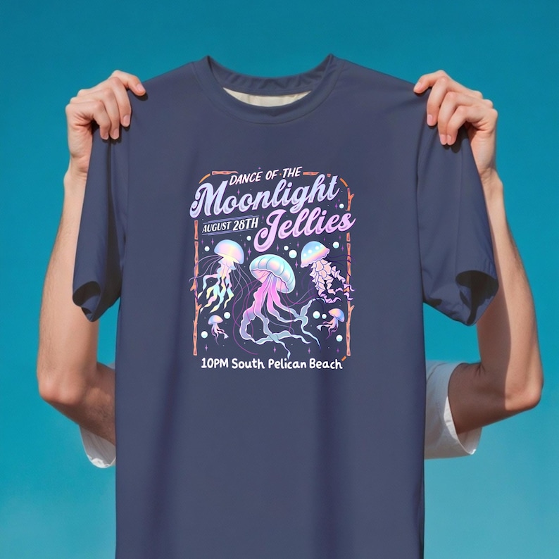 May include: Navy blue t-shirt featuring a graphic of jellyfish in shades of pink, purple, and blue. The text reads "Dance of the Moonlight Jellies, August 28th, 10PM South Pelican Beach."