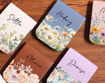 May include: Five floral-themed magnetic bookmarks with names: Sella, Hedwig, Merry, Olivia, and Denise. Each bookmark features a different floral design and color scheme, including daisies, roses, and wildflowers. The bookmarks are arranged on a wooden surface.