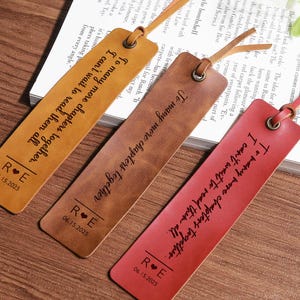Pode incluir: Três marcadores de livros de couro em tons de bege, castanho e vermelho, cada um com um cordão de couro. Os marcadores de livros têm o texto "To many more chapters together. I can't wait to read them all." e iniciais com uma data.