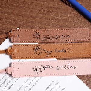 Może przedstawiać: Trzy spersonalizowane skórzane zakładki do książek w odcieniach brązu i różu. Każda zakładka ma kwiatowy wzór i imię: Sofia, Candy i Dallas. Niebieski długopis leży w tle.