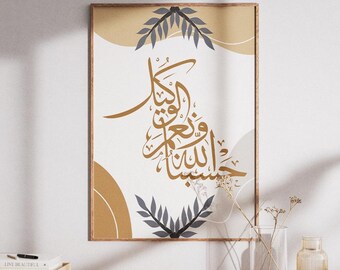 May include: A framed art print featuring Arabic calligraphy in gold against a white background with abstract shapes in beige and gray. Decorative gray leaves are at the top and bottom. The print is displayed on a wooden surface.