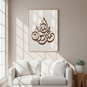 Puede incluir: Impresión artística enmarcada con caligrafía árabe marrón sobre fondo crema. La obra de arte se presenta en un marco dorado, añadiendo un toque de elegancia. Esta impresión decorativa es adecuada para la decoración de interiores.