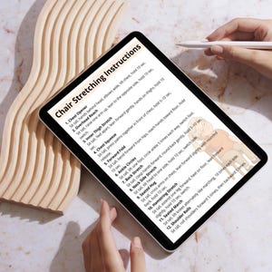 May include: A digital tablet displays "Chair Stretching Instructions" with a list of exercises. The tablet is held by a person, and a stylus is visible. The background features a light-colored wooden decorative element.