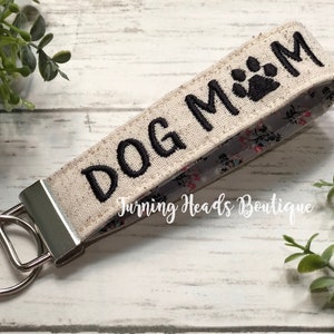 May include: A beige fabric key chain with a black embroidered paw print and the text "DOG MOM".