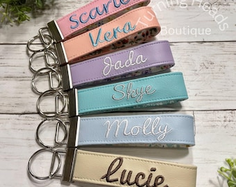 May include: A set of six personalized keychains made of faux leather in pastel colors including pink, peach, lavender, teal, light blue, and cream. Each keychain features a silver metal ring and embroidered names: Scarlett, Vera, Jada, Skye, Molly, and Lucie.