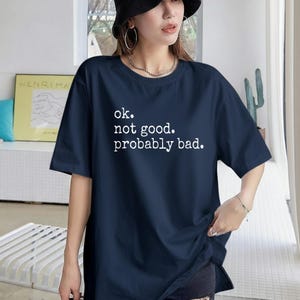 May include: Navy blue t-shirt with the text "ok. not good. probably bad." in white. The shirt has short sleeves and a crew neck. The shirt is a casual style.