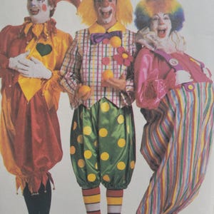 May include: Three clown costumes featuring vibrant colours and patterns. The first is a red and yellow jester-style outfit with a heart patch. The second is a plaid vest with green polka-dot trousers. The third is a pink top with striped trousers.
