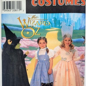 Pode incluir: Molde de costura Simplicity Costumes 7801 para O Mágico de Oz. A embalagem apresenta ilustrações de um traje de bruxa preto, um vestido xadrez azul e branco e um vestido rosa com estrelas e uma coroa alta, junto com um pequeno cão preto.