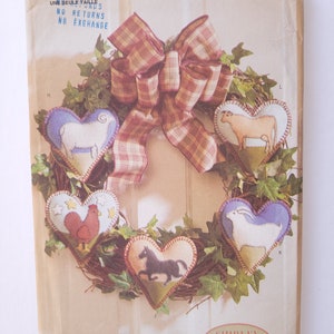 Puede incluir: Un sobre de patrón Butterick con una corona en forma de corazón con aplicaciones de animales de granja. La corona tiene un lazo a cuadros y está rodeada de vegetación. El texto "5861" y "Butterick" son visibles.
