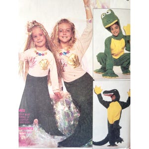 May include: Image of children's costumes. Two girls are dressed as mermaids, wearing long-sleeved shirts with seashell designs and dark green skirts. Other costumes include a frog and an alligator. The image is from a vintage sewing pattern.