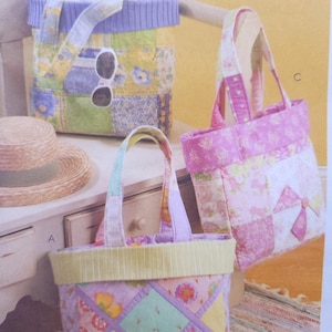 Op de afbeelding: Drie handgemaakte stoffen draagtassen en een trekkoordtas met bloemenpatchworkontwerpen. De tassen hebben verschillende kleuren, waaronder roze, geel, groen en paars. Eén tas heeft een zonnebril.