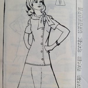 Può includere: Disegno a tratto di una donna con un abito abbottonato con fiocco al collo. L'abito ha maniche corte e una gonna svasata. Una piccola illustrazione dell'abito è in alto. Testo con misure.