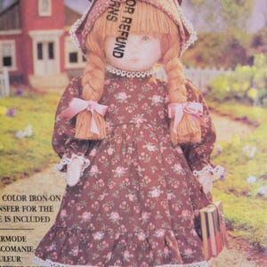 May include: A vintage doll from the Vogue Doll Collection, wearing a floral print dress with a matching bonnet and pink bows. The doll has long, braided hair and is holding a small, striped purse. The doll is designed by Linda Carr.
