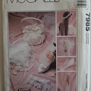 May include: A McCall's pattern for a wedding accessory set, including a bridal bouquet, a garter, a ring pillow, a flower girl basket, gloves, and a hairpiece. The pattern is called "Alicyn Exclusives" and the pattern number is 7985.