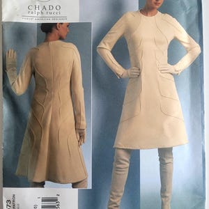 Pode incluir: Um padrão Vogue para um vestido Chado Ralph Rucci. O vestido é de cor bege claro com mangas compridas, uma saia rodada e costuras decorativas. O padrão inclui um casaco e luvas a condizer. A modelo usa botas altas.