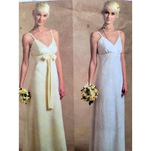 Puede incluir: Dos mujeres modelan vestidos de novia. El vestido de la izquierda es de color crema claro con un lazo en la cintura. El vestido de la derecha es blanco con un patrón texturizado. Ambos vestidos tienen tirantes finos y cuello en V. Cada mujer sostiene un ramo.