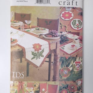 May include: A Vogue Craft pattern featuring various Christmas-themed craft projects. The image showcases a table runner, coasters, chair decorations, and ornaments, all with festive poinsettia and holly designs. The pattern includes the text "7465" and "Texas Design Studio".