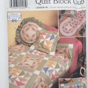 Pode incluir: Padrão Simplicity Quilt Block Club com um design Double Wedding Ring & Dutchman's Puzzle. A imagem mostra um edredom, uma almofada e um caminho de mesa com padrões geométricos coloridos. O padrão é da Shirley Botsford Designs.