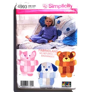 Puede incluir: Patrón de manualidades Simplicity 4993 con una colcha infantil y tres diseños de animales de peluche: un oso rosa y blanco, un perro azul y blanco y un oso marrón y naranja. El patrón incluye el texto "Fabricland No Returns or Exchanges."