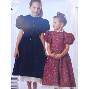 May include: Two girls in dresses. One is navy blue with a white lace collar and hem. The other is red with a floral pattern, a white lace collar and hem. Both dresses have puffed sleeves.