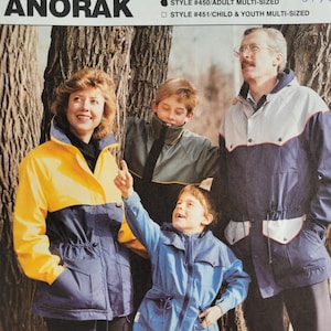 May include: Anorak sewing pattern featuring a family wearing jackets. The pattern includes adult and child sizes. The jackets are in blue, yellow, and gray. The text on the pattern reads "Anorak" and "Complete Full Size Patterns".